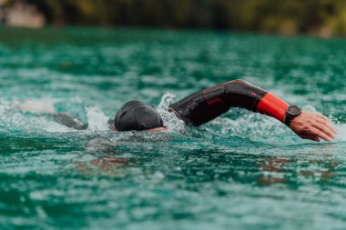 A triathlete in a professional swimming suit trains on the river while preparing for Olympic swimming. 