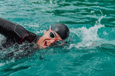 A triathlete in a professional swimming suit trains on the river while preparing for Olympic swimming. 