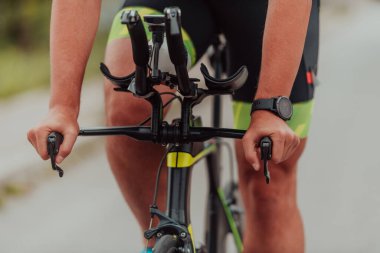 Close up photo of an active triathlete in sportswear and with a protective helmet riding a bicycle. Selective focus. 