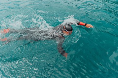A triathlete in a professional swimming suit trains on the river while preparing for Olympic swimming. 