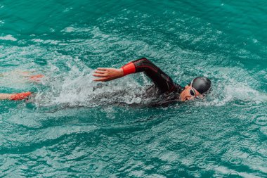 A triathlete in a professional swimming suit trains on the river while preparing for Olympic swimming. 
