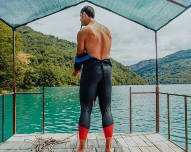 Athlete putting on a swimming suit and preparing for triathlon swimming and training in the river surrounded by natural greenery. 