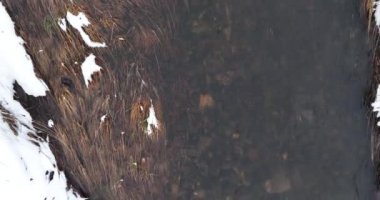 An aerial view of a frozen river flowing through snow-covered forests on a cloudy sunset sky background. Hi quality 4K footage.