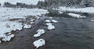 An aerial view of a frozen river flowing through snow-covered forests on a cloudy sunset sky background. Hi quality 4K footage.