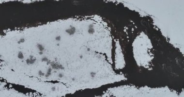 An aerial view of a frozen river flowing through snow-covered forests on a cloudy sunset sky background. Hi quality 4K footage.