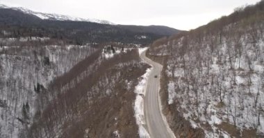Aerial view of mountain twisted road in the winter. Epic, snowy white winter in the mountains. High rocky mountains and clean road through frozen forest. High quality 4k footage