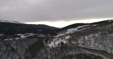 Aerial view of mountain twisted road in the winter. Epic, snowy white winter in the mountains. High rocky mountains and clean road through frozen forest. High quality 4k footage