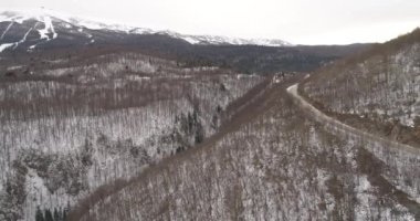 Aerial view of mountain twisted road in the winter. Epic, snowy white winter in the mountains. High rocky mountains and clean road through frozen forest. High quality 4k footage