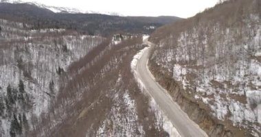Aerial view of mountain twisted road in the winter. Epic, snowy white winter in the mountains. High rocky mountains and clean road through frozen forest. High quality 4k footage