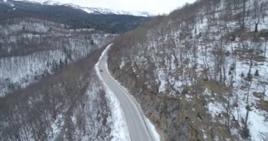 Aerial view of mountain twisted road in the winter. Epic, snowy white winter in the mountains. High rocky mountains and clean road through frozen forest. High quality 4k footage