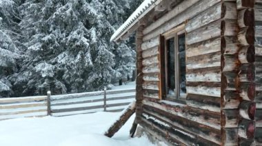 Splendid mountain winter landscape with secluded small wooden alpine cottage among the fir trees fully covered by snow during snow fall. Hi quality 4K slow motion footage. 