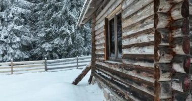 Splendid mountain winter landscape with secluded small wooden alpine cottage among the fir trees fully covered by snow during snow fall. Hi quality 4K slow motion footage. 