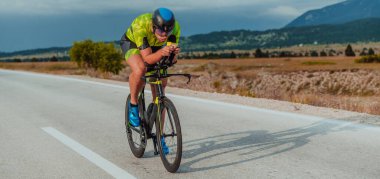 Full length portrait of an active triathlete in sportswear and with a protective helmet riding a bicycle. Selective focus.