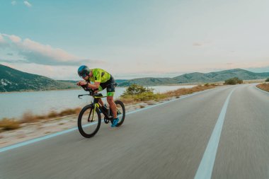 Full length portrait of an active triathlete in sportswear and with a protective helmet riding a bicycle. Selective focus.