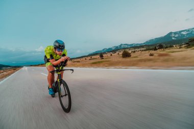 Full length portrait of an active triathlete in sportswear and with a protective helmet riding a bicycle. Selective focus.