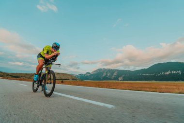 Full length portrait of an active triathlete in sportswear and with a protective helmet riding a bicycle. Selective focus.