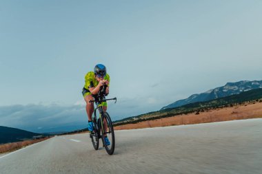 Full length portrait of an active triathlete in sportswear and with a protective helmet riding a bicycle. Selective focus.