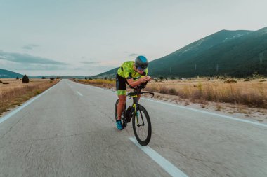 Full length portrait of an active triathlete in sportswear and with a protective helmet riding a bicycle. Selective focus.