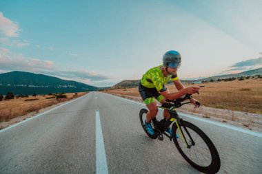 Full length portrait of an active triathlete in sportswear and with a protective helmet riding a bicycle. Selective focus.