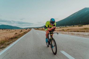 Full length portrait of an active triathlete in sportswear and with a protective helmet riding a bicycle. Selective focus.