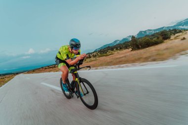 Full length portrait of an active triathlete in sportswear and with a protective helmet riding a bicycle. Selective focus.