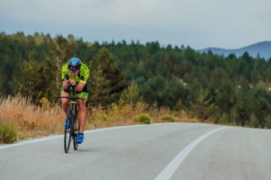 Full length portrait of an active triathlete in sportswear and with a protective helmet riding a bicycle. Selective focus.