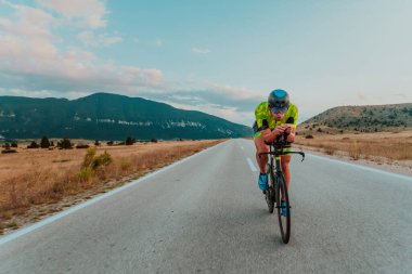 Full length portrait of an active triathlete in sportswear and with a protective helmet riding a bicycle. Selective focus.