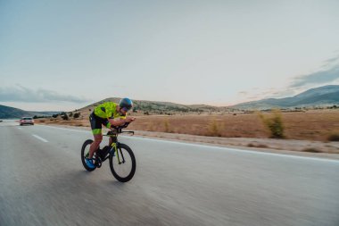 Full length portrait of an active triathlete in sportswear and with a protective helmet riding a bicycle. Selective focus.