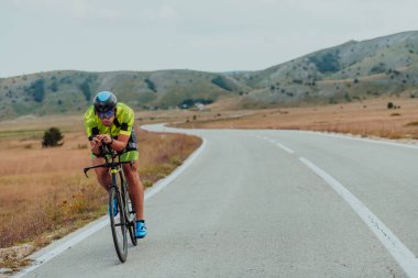 Full length portrait of an active triathlete in sportswear and with a protective helmet riding a bicycle. Selective focus.