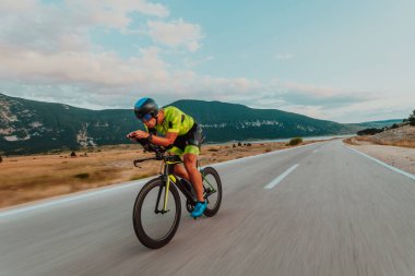 Full length portrait of an active triathlete in sportswear and with a protective helmet riding a bicycle. Selective focus.