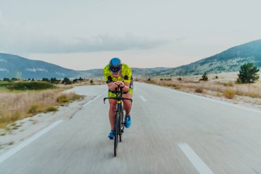 Full length portrait of an active triathlete in sportswear and with a protective helmet riding a bicycle. Selective focus.