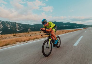 Full length portrait of an active triathlete in sportswear and with a protective helmet riding a bicycle. Selective focus.