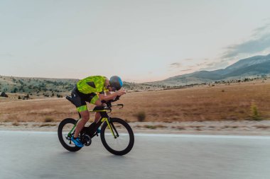 Full length portrait of an active triathlete in sportswear and with a protective helmet riding a bicycle. Selective focus.