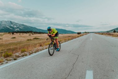 Full length portrait of an active triathlete in sportswear and with a protective helmet riding a bicycle. Selective focus.