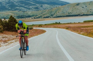 Full length portrait of an active triathlete in sportswear and with a protective helmet riding a bicycle. Selective focus.
