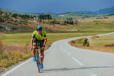 Full length portrait of an active triathlete in sportswear and with a protective helmet riding a bicycle. Selective focus.