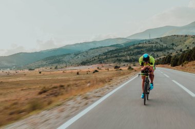 Full length portrait of an active triathlete in sportswear and with a protective helmet riding a bicycle. Selective focus.