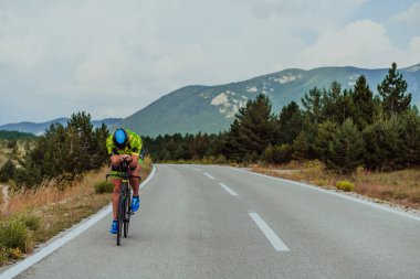 Full length portrait of an active triathlete in sportswear and with a protective helmet riding a bicycle. Selective focus.