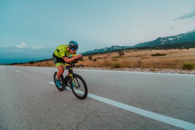 Full length portrait of an active triathlete in sportswear and with a protective helmet riding a bicycle. Selective focus.