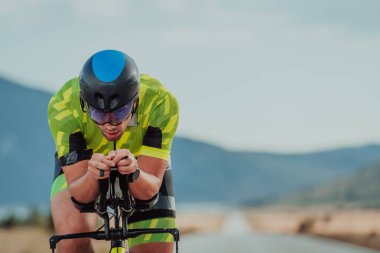 Close up photo of an active triathlete in sportswear and with a protective helmet riding a bicycle. Selective focus. 