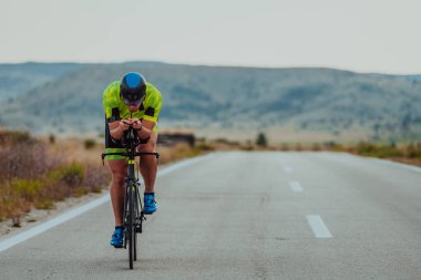 Full length portrait of an active triathlete in sportswear and with a protective helmet riding a bicycle. Selective focus.