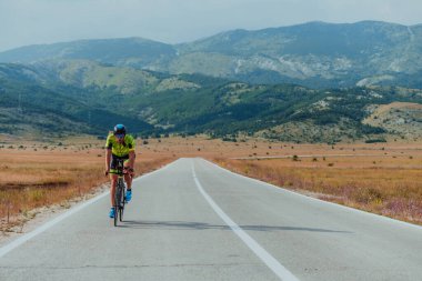 Full length portrait of an active triathlete in sportswear and with a protective helmet riding a bicycle. Selective focus.