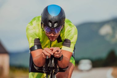 Close up photo of an active triathlete in sportswear and with a protective helmet riding a bicycle. Selective focus. 