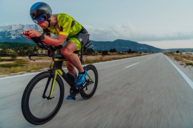 Full length portrait of an active triathlete in sportswear and with a protective helmet riding a bicycle. Selective focus.