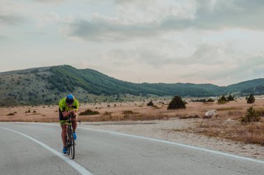 Full length portrait of an active triathlete in sportswear and with a protective helmet riding a bicycle. Selective focus.