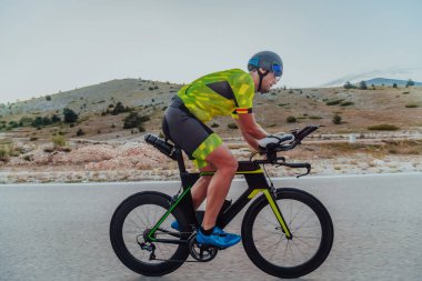 Full length portrait of an active triathlete in sportswear and with a protective helmet riding a bicycle. Selective focus.