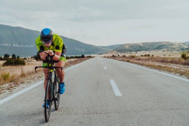 Full length portrait of an active triathlete in sportswear and with a protective helmet riding a bicycle. Selective focus.