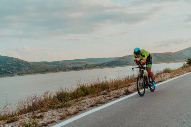 Full length portrait of an active triathlete in sportswear and with a protective helmet riding a bicycle. Selective focus.