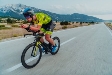 Full length portrait of an active triathlete in sportswear and with a protective helmet riding a bicycle. Selective focus.