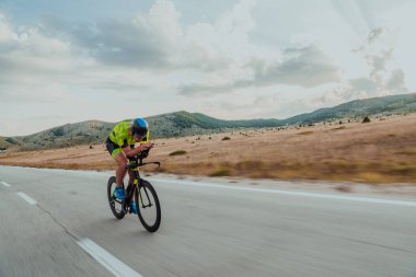 Full length portrait of an active triathlete in sportswear and with a protective helmet riding a bicycle. Selective focus.